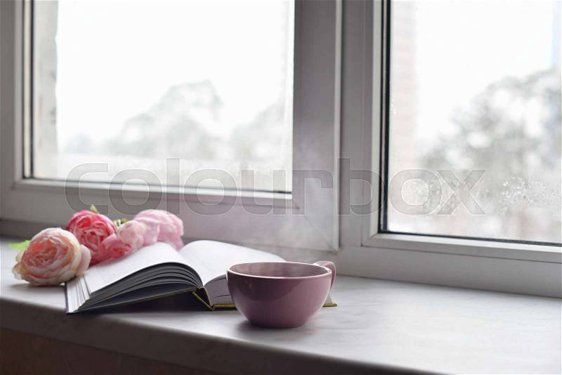 Cozy home still life: cup of hot coffee, spring flowers and opened book with warm plaid on windowsill against snow landscape outside. Springtime concept, free copy space, stock photo