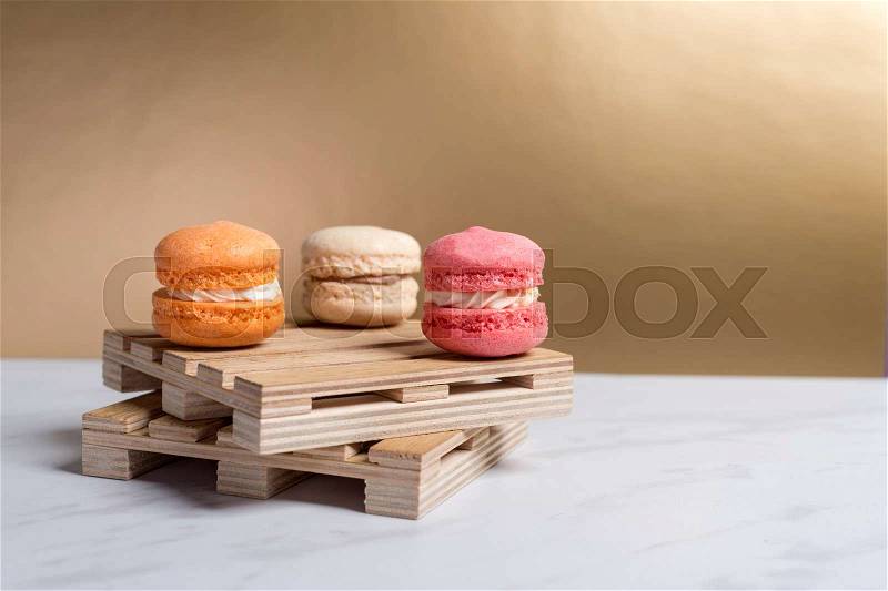 Sweet and colourful macaroons served on little wooden pallets on a marble texture table and golden background. Traditional french dessert. Copy space, stock photo