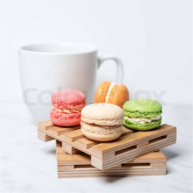Sweet and colourful macaroons served on little wooden pallets with cup of coffee on a marble texture background. Traditional french dessert, stock photo