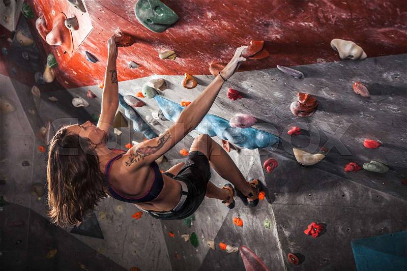 Young woman training on practice climbing wall indoor, stock photo
