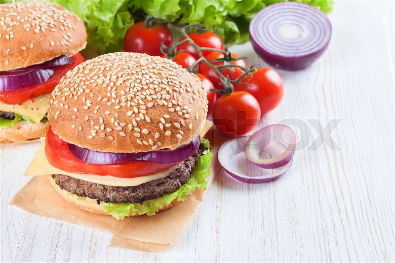 Homemade cheeseburger with beef patties, fresh salad, tomatoes and onion on seasame buns, served on white wooden table, stock photo