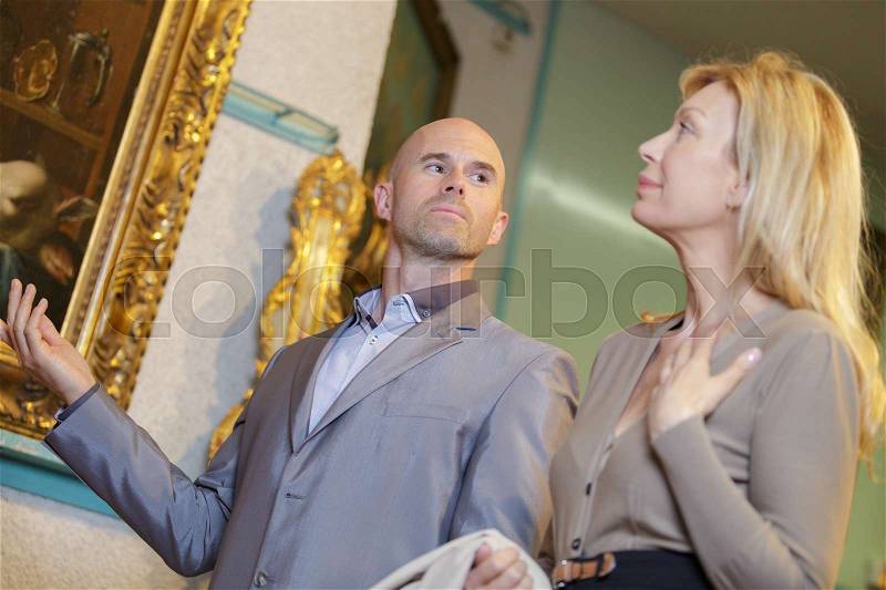 Smiling mature woman choosing picture at the art gallery, stock photo