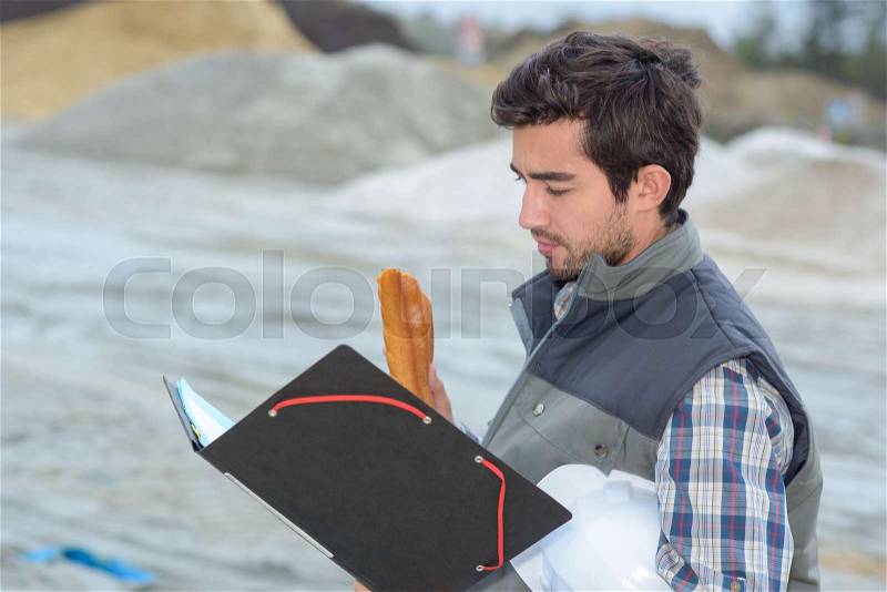 Man on construction site holding file and baguette, stock photo