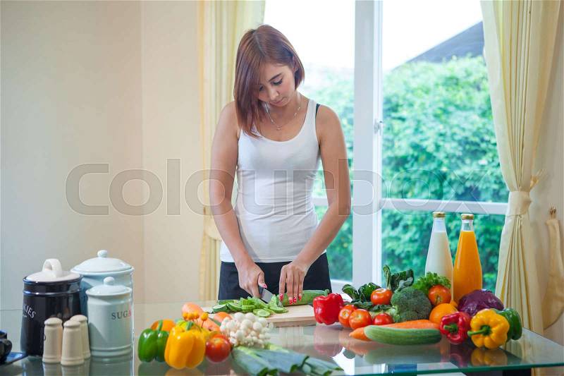 Happy asian woman cooking vegetables green salad in the kitchen, stock photo
