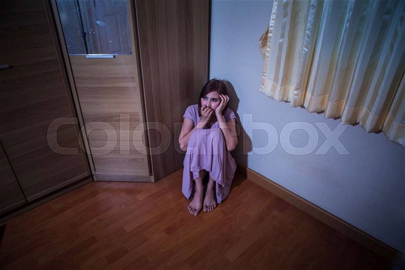 Scared abused woman sitting in the corner of the room, stock photo