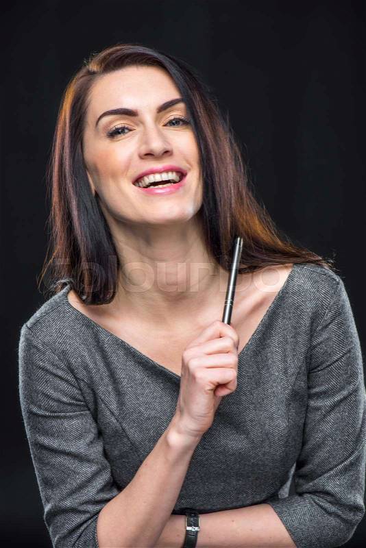 Laughing young woman holding pen and looking at camera on black, stock photo