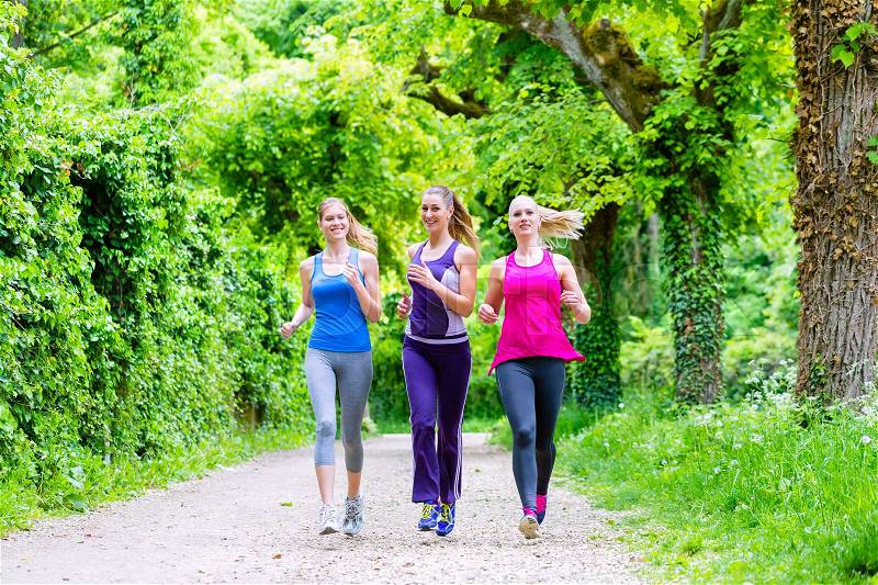Three motivated women jogging in green forest, stock photo