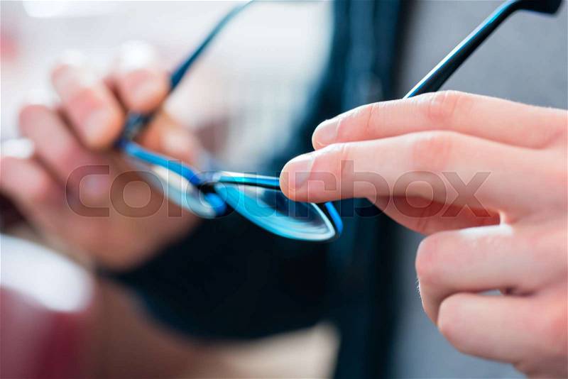 Man testing glasses at optician shop in his hand, stock photo