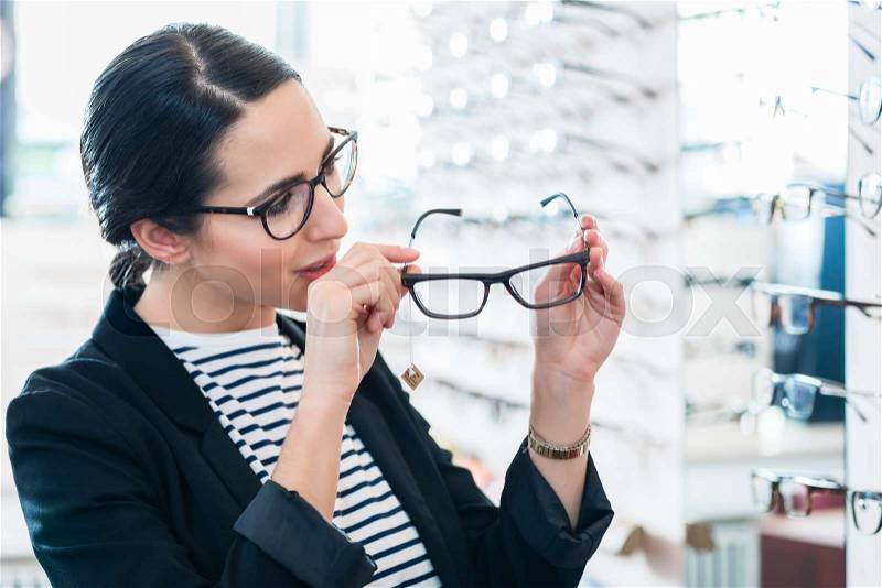 Woman taking glasses off shelf in optician shop, stock photo