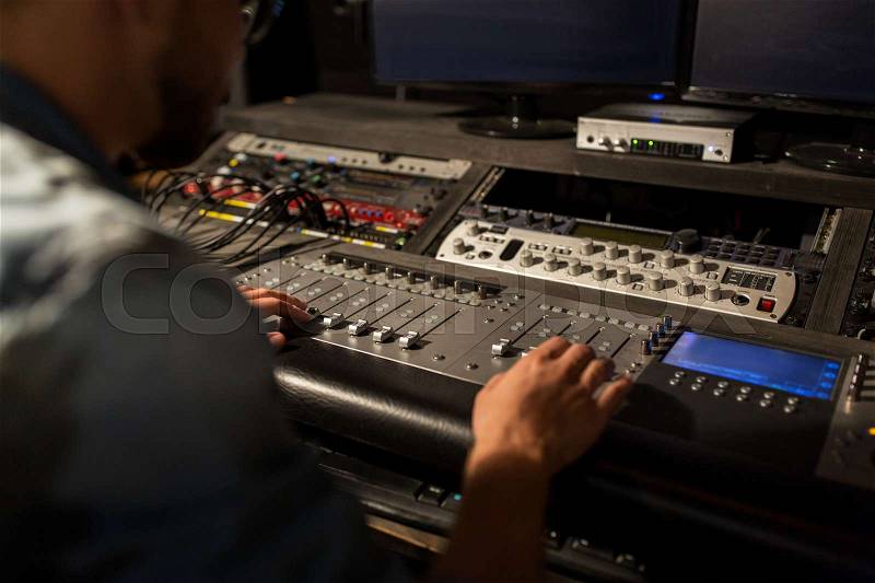 Music, technology, people and equipment concept - man using mixing console in sound recording studio, stock photo