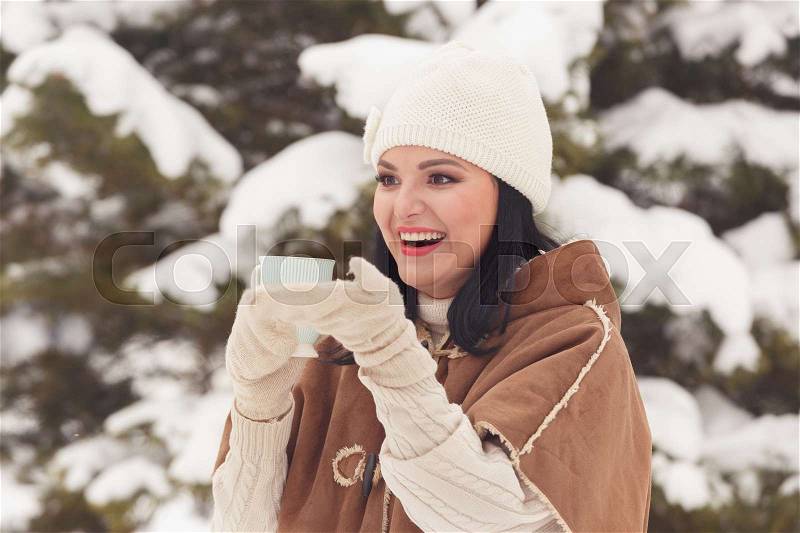 Beautiful woman in warm clothes holding coffee or tea, looking forward happy and smiling outdoors in a sunny winter day, vintage toning, stock photo