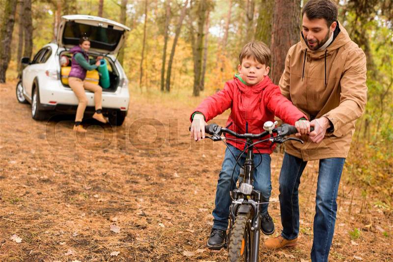 Happy father teaching his son to ride a bicycle in autumn forest, stock photo