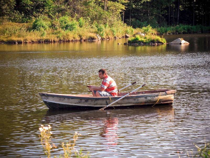 A young man fishing out of a row boat Stock Photo
