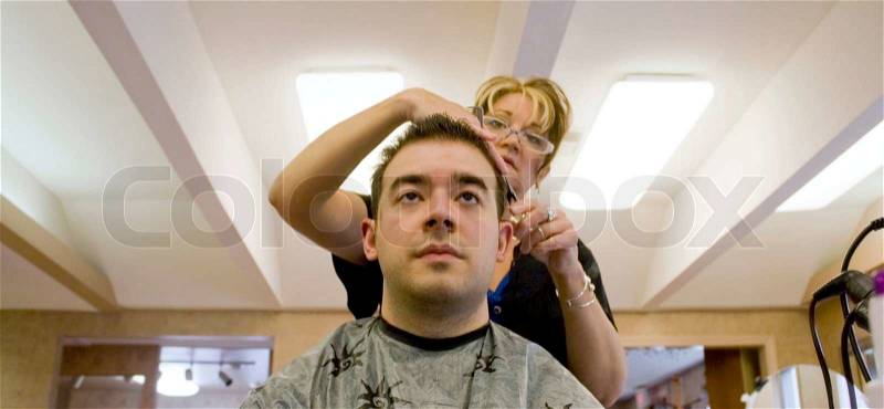 A young man is getting his hair cut by a hairdresser at the salon, stock photo