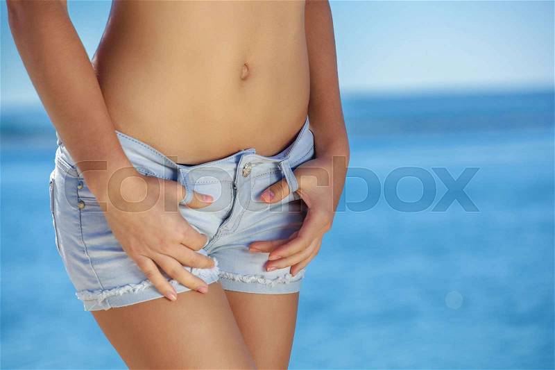 Young, skinny, pretty girl in denim blue shorts on the beach, the sea. Dropping e overweight, stock photo