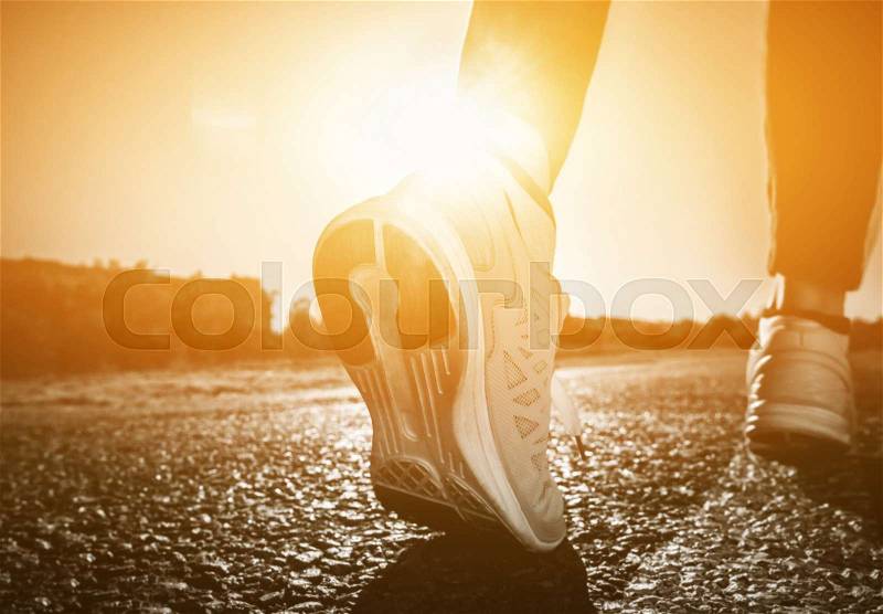 Young athlete in sneakers makes summer morning workout and exercises. Running on the move close-up on a background of the rising sun. Sports and healthy lifestyle, stock photo