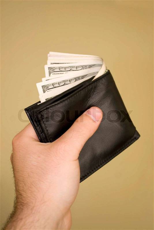 A hand holding a wallet full of cash isolated over a gold background, stock photo