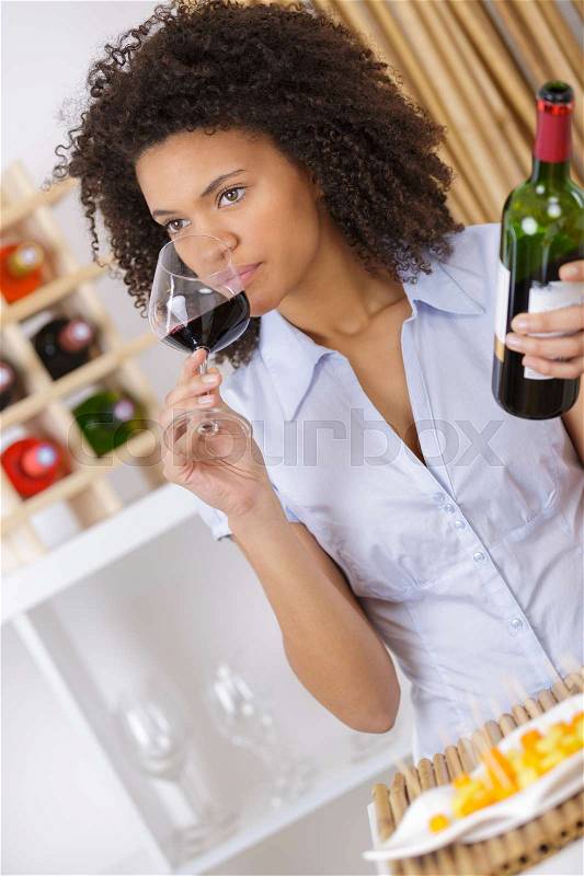 Woman tasting wine in glass and holding bottle, stock photo