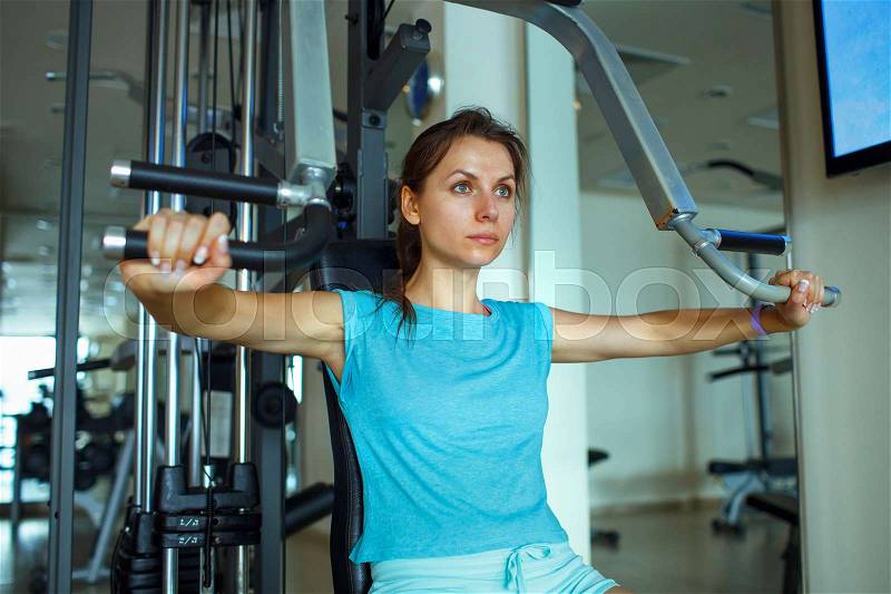 Athletic woman works out on training apparatus in fitness center, stock photo