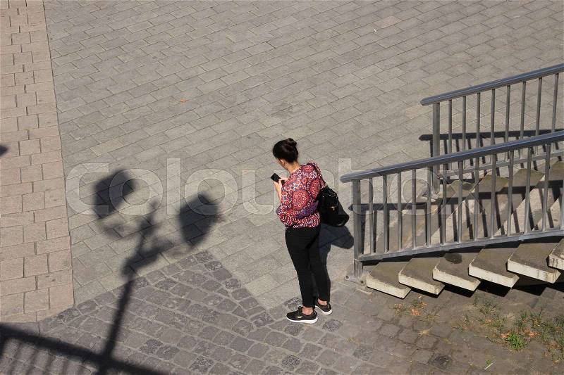 Shadow of the streetlights, steps and a lady is watching on her mobile phone in the shopping centre of the city in the wonderful summer, stock photo