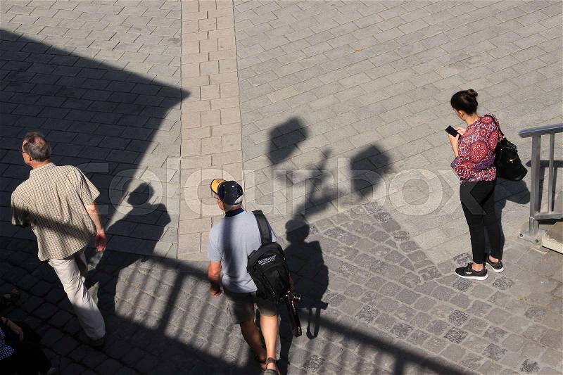Two men are walking, shadow of the streetlights and a lady is watching on her mobile phone in the shopping centre of the city in the wonderful summer, stock photo