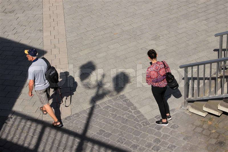 Shadow of the streetlights, steps, a photographer is walking and a lady is watching on her mobile phone in the shopping centre of the city in the wonderful summer, stock photo