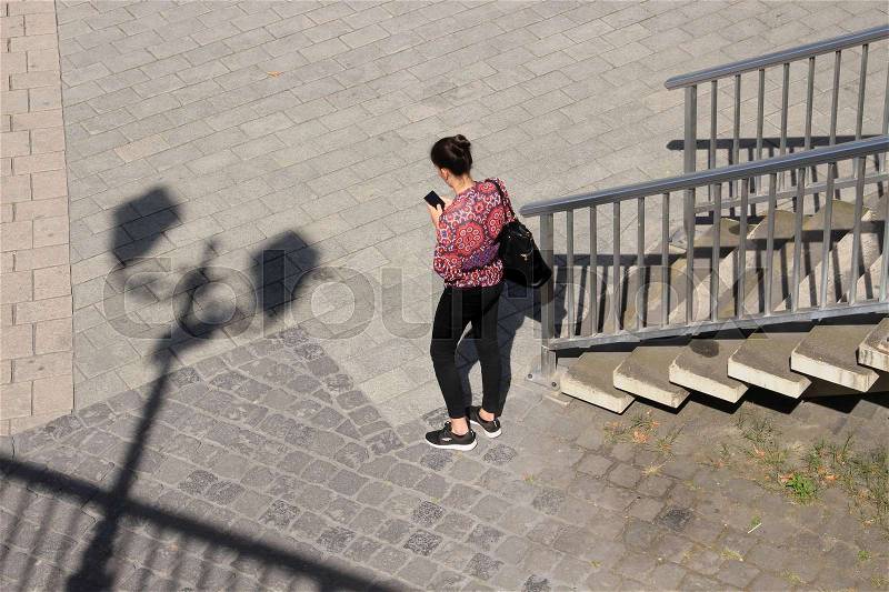 Shadow of the streetlights, steps and a lady is watching on her mobile phone in the shopping centre of the city in the wonderful summer, stock photo