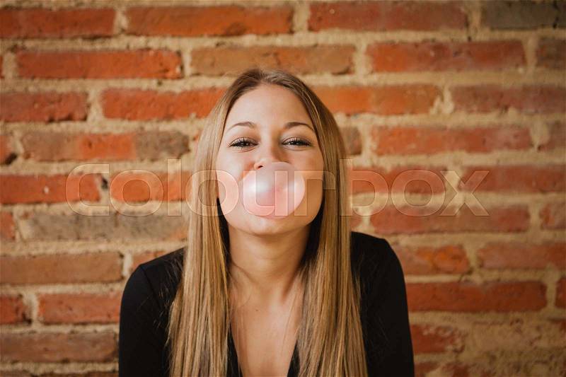 Funny girl making a pomp with a bubble gum and a brick wall of background, stock photo