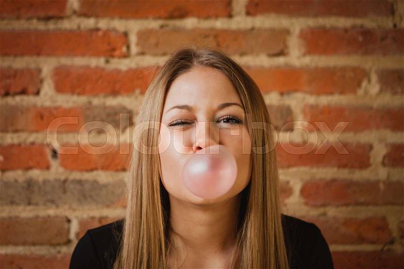 Funny girl making a pomp with a bubble gum and a brick wall of background, stock photo