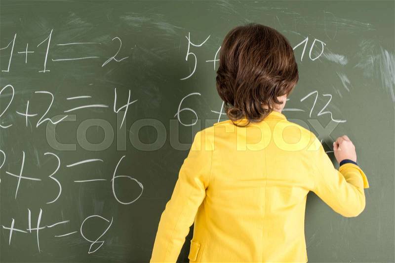 Back view of schoolboy writing with chalk on blackboard, stock photo
