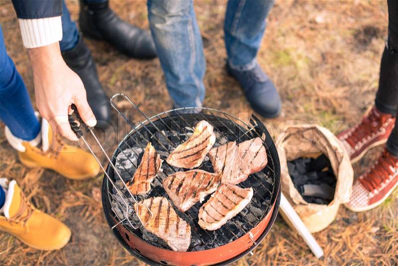 Close-up view of young people grilling meat on a charcoal grill outdoors, stock photo