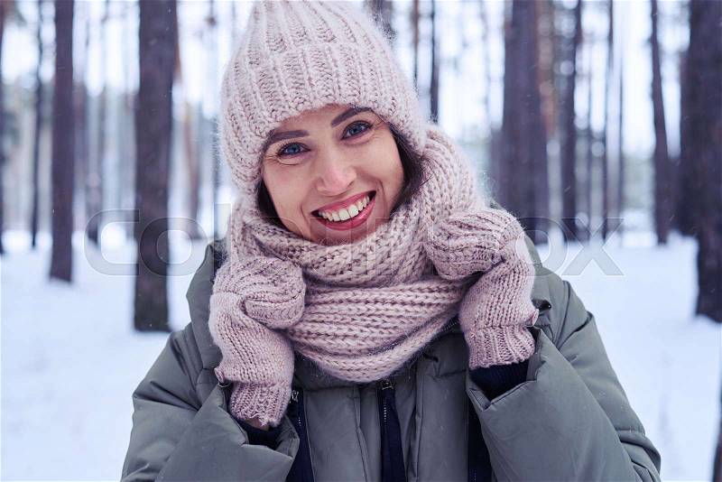 Close-up of exquisite smile of woman during the wintry walk in the forest. Fashion portrait of a beautiful Caucasian woman in a winter forest, stock photo