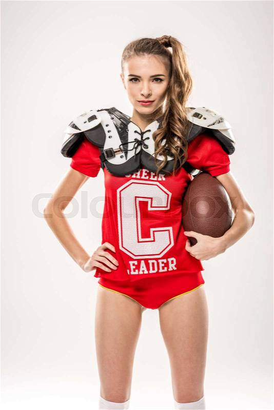 Beautiful female american football player posing with ball on grey, stock photo