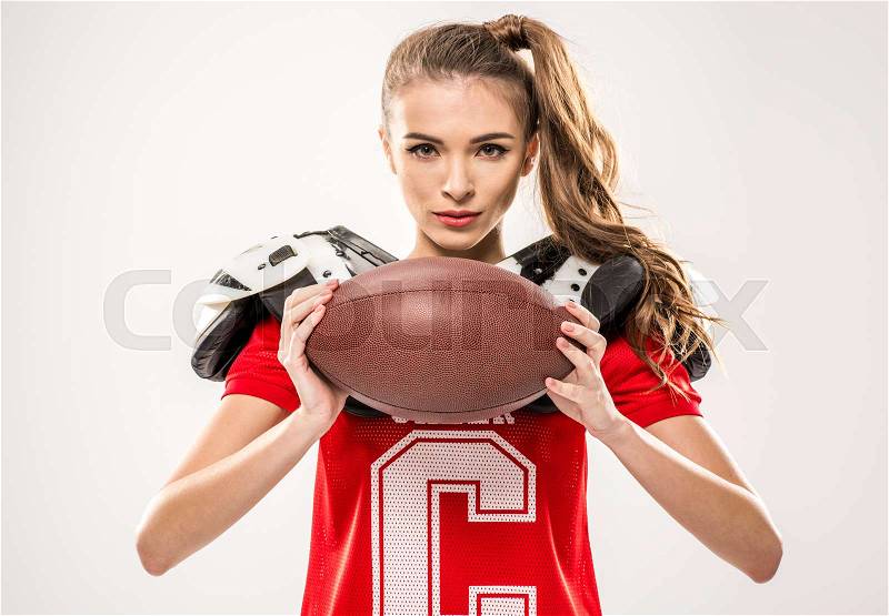 Beautiful female american football player posing with ball on grey, stock photo