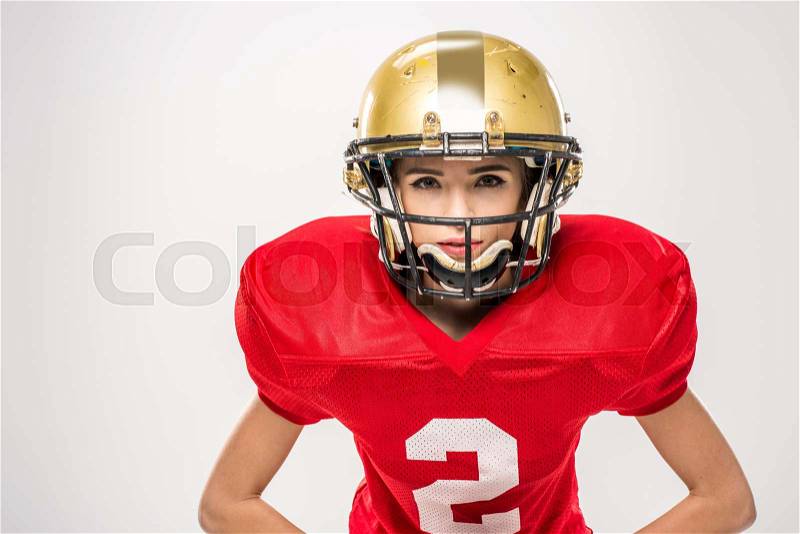 Beautiful female american football player in helmet posing with ball on grey, stock photo