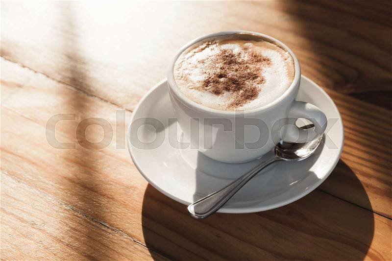 Cappuccino. Cup of coffee with milk foam and cinnamon stands on wooden table in morning sunlight, stock photo