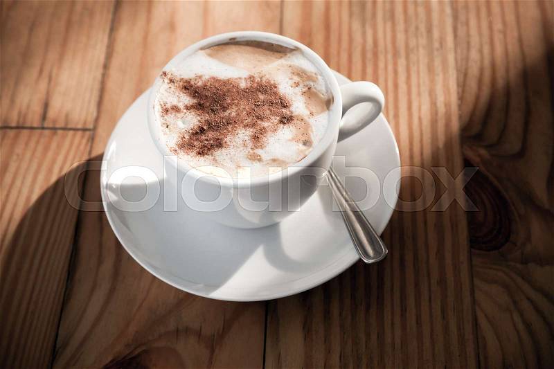 Cappuccino. Cup of coffee with milk foam and cinnamon powder stands on wooden table in morning sunlight, stock photo