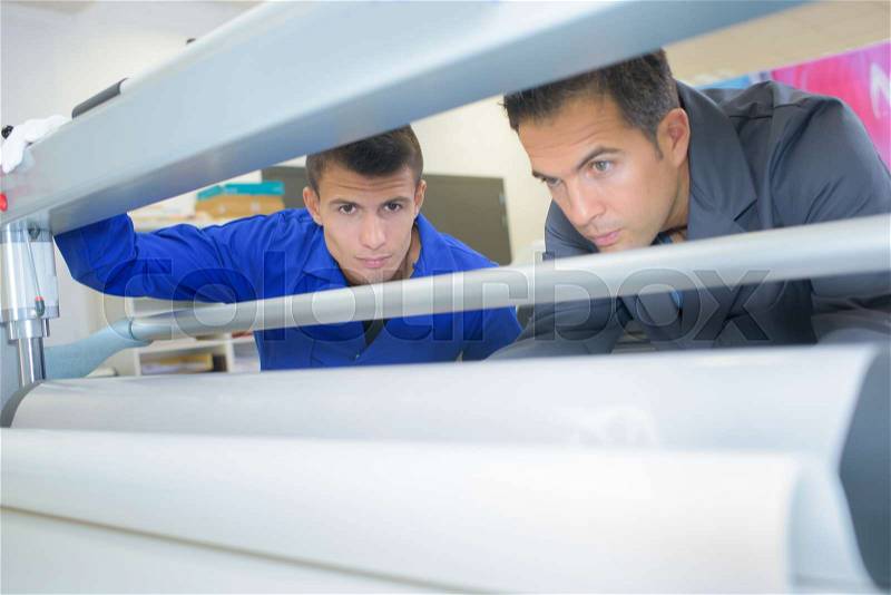 Two men working on industrial printing machine, stock photo