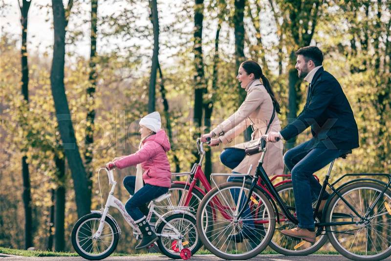 Side view of happy family riding bikes in autumn park, stock photo