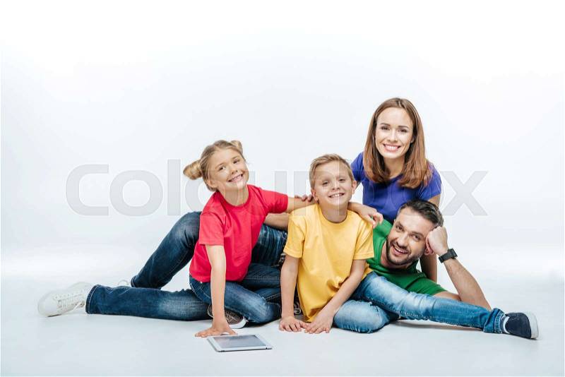 Happy family in colored t-shirts lying together with digital tablet, stock photo