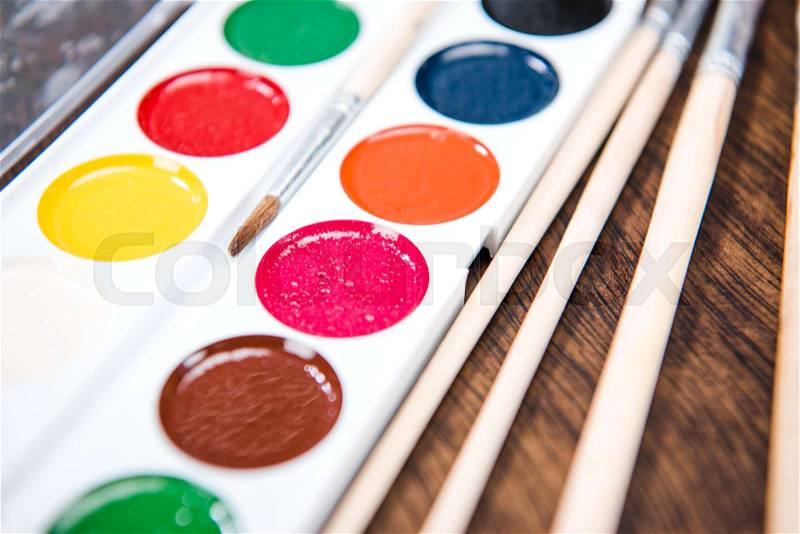 Close-up view of watercolor paints and paintbrushes on wooden table, stock photo