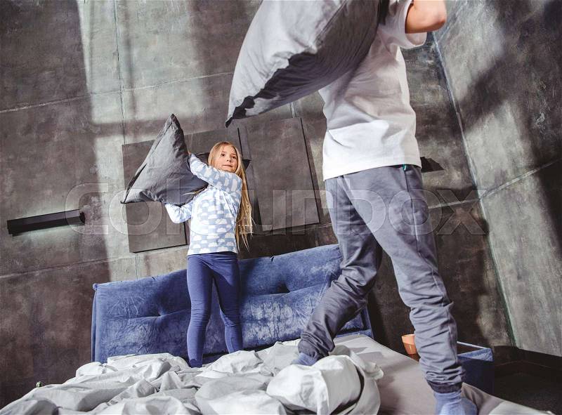 Cute siblings fighting with pillows on bed in bedroom, stock photo
