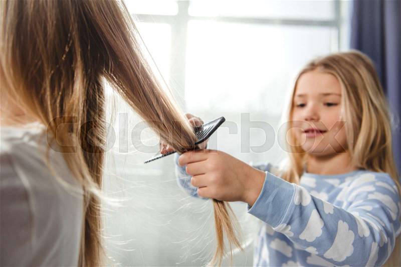 Smiling little daughter combing hair of her mother, stock photo