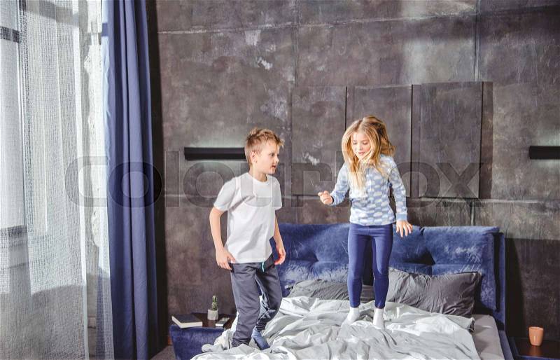 Happy siblings jumping on bed in bedroom, stock photo