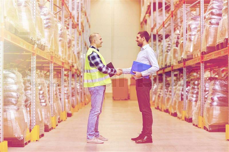 Wholesale, logistic, people and export concept - manual worker and businessmen with clipboard shaking hands and making deal at warehouse, stock photo