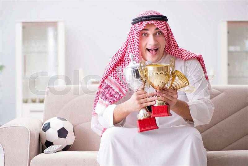 Young arab man watching football sitting on sofa, stock photo