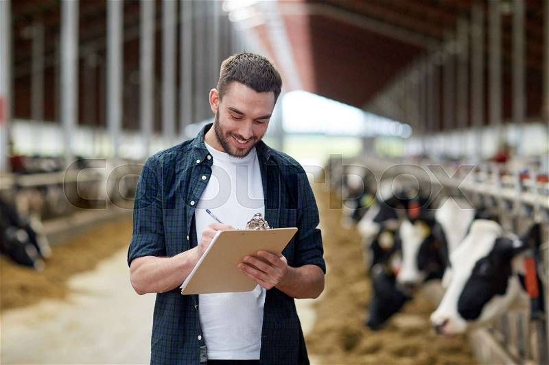 Agriculture industry, farming, people and animal husbandry concept - happy smiling young man or farmer with clipboard and cows in cowshed on dairy farm, stock photo
