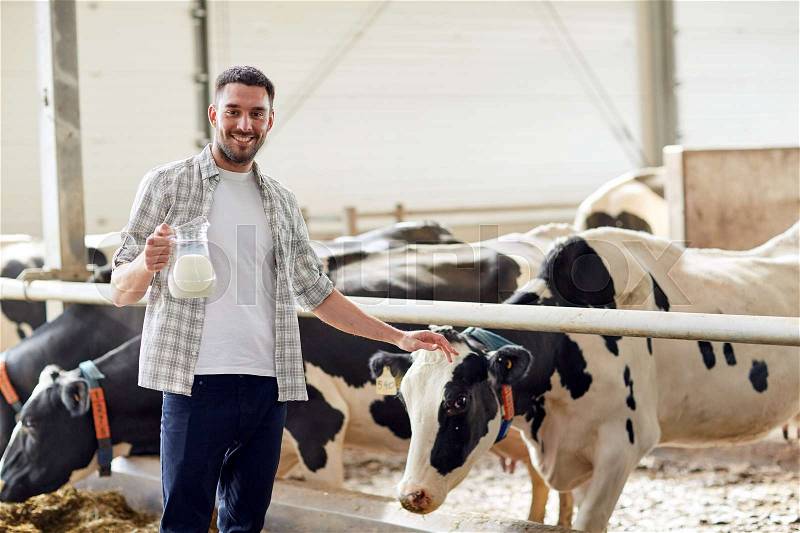 Agriculture industry, farming, people and animal husbandry concept - happy smiling young man or farmer with cows milk in jug at cowshed on dairy farm, stock photo