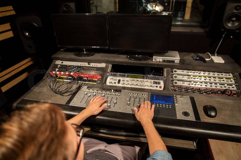 Music, technology, people and equipment concept - man at mixing console in sound recording studio, stock photo