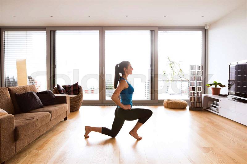 Beautiful young woman working out at home in living room, doing yoga or pilates exercise, stretching legs, stock photo